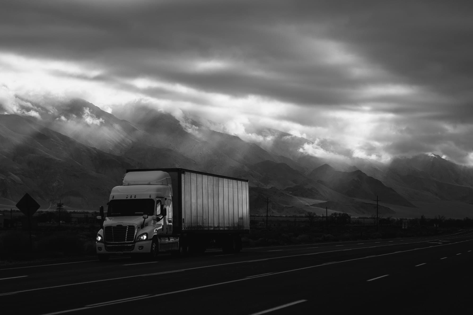 A Freightliner Cascadia tractor-trailer on a US highway beneath storm cloud